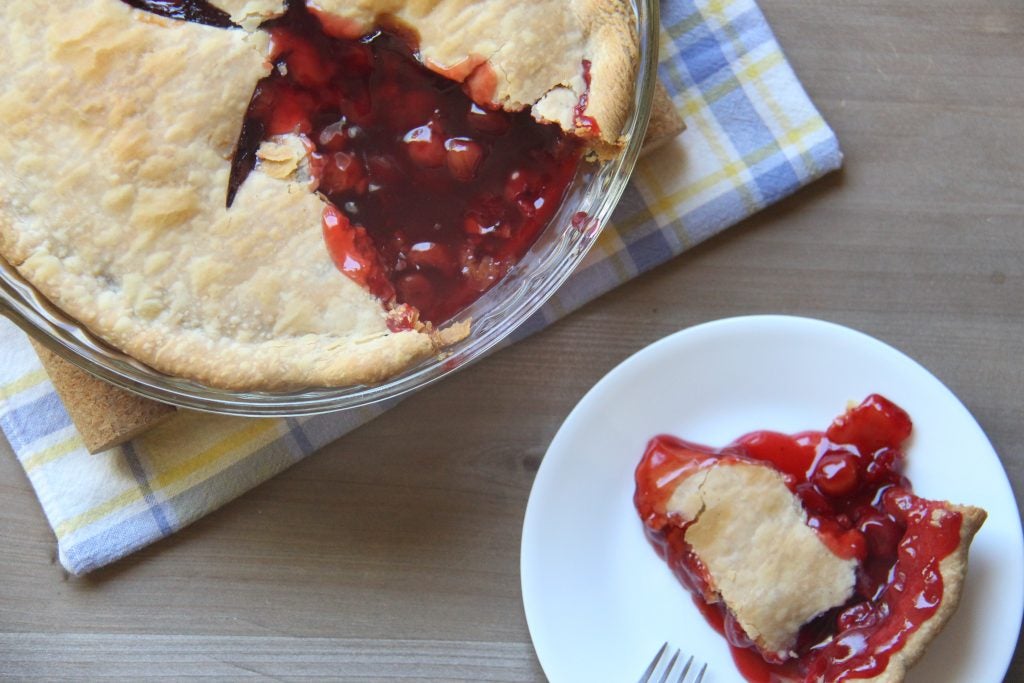 A cherry pie with one slice removed and placed on a small, circular dish.