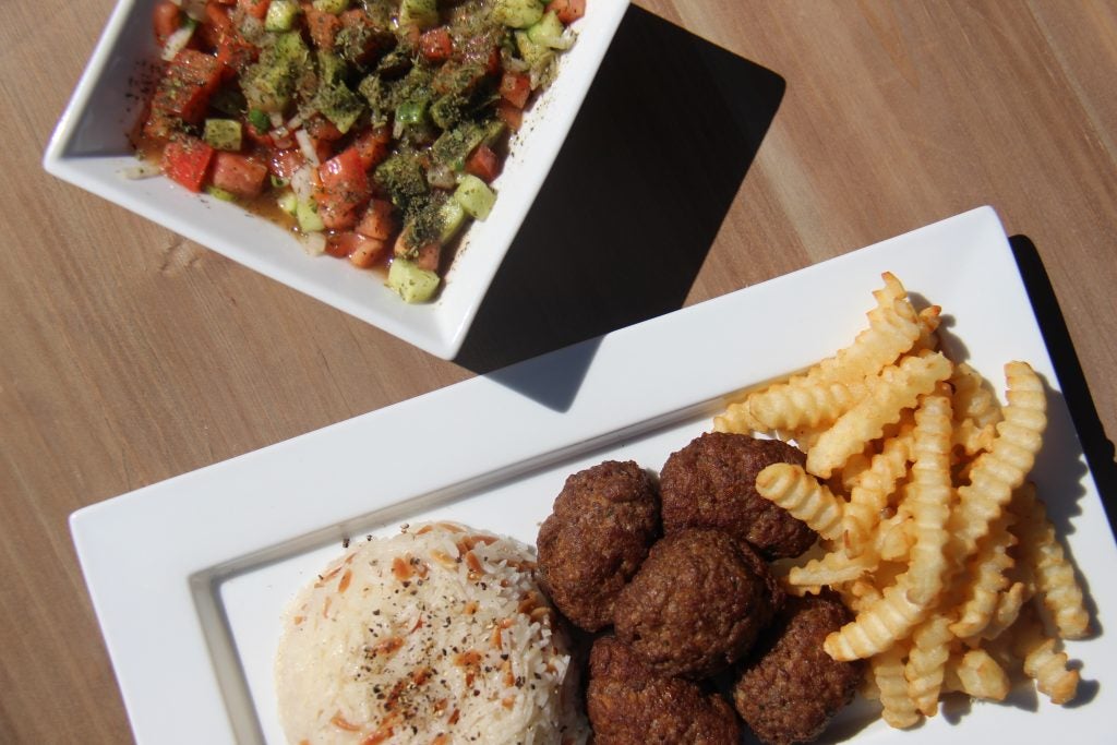 Turkish meatballs, pilav, and french fries served on a rectangular dish, placed next to a serving of salad.