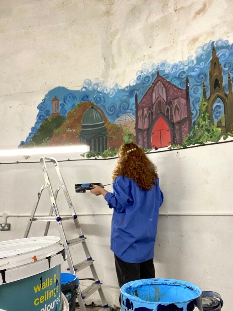 Nell is observing her mural on the walls of the Bedlam Theater.