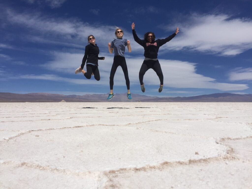 Thee students mid jump over salt flats.