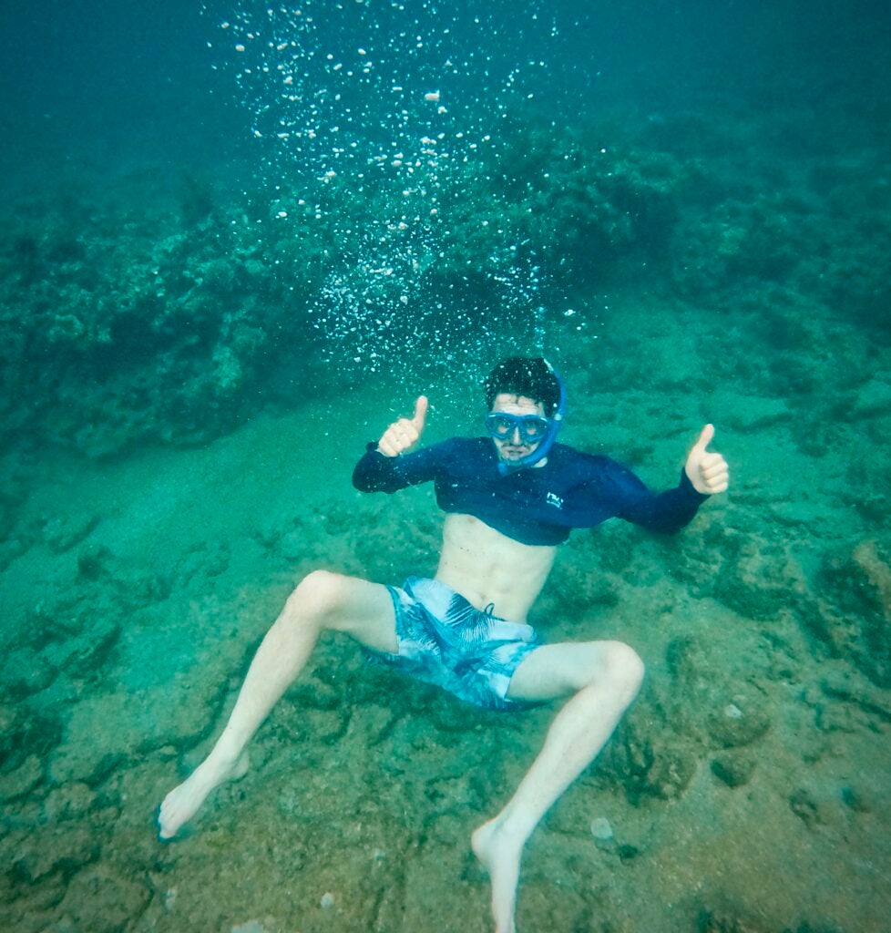 John snorkeling in the water, holding two thumbs up