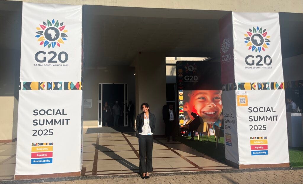 Girl stands in between banners that read "G20 Social Summit 2025."