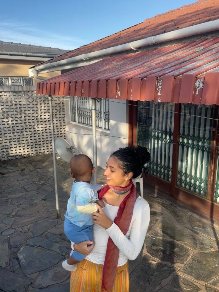 Girl holding a baby in front of a house under a red roof