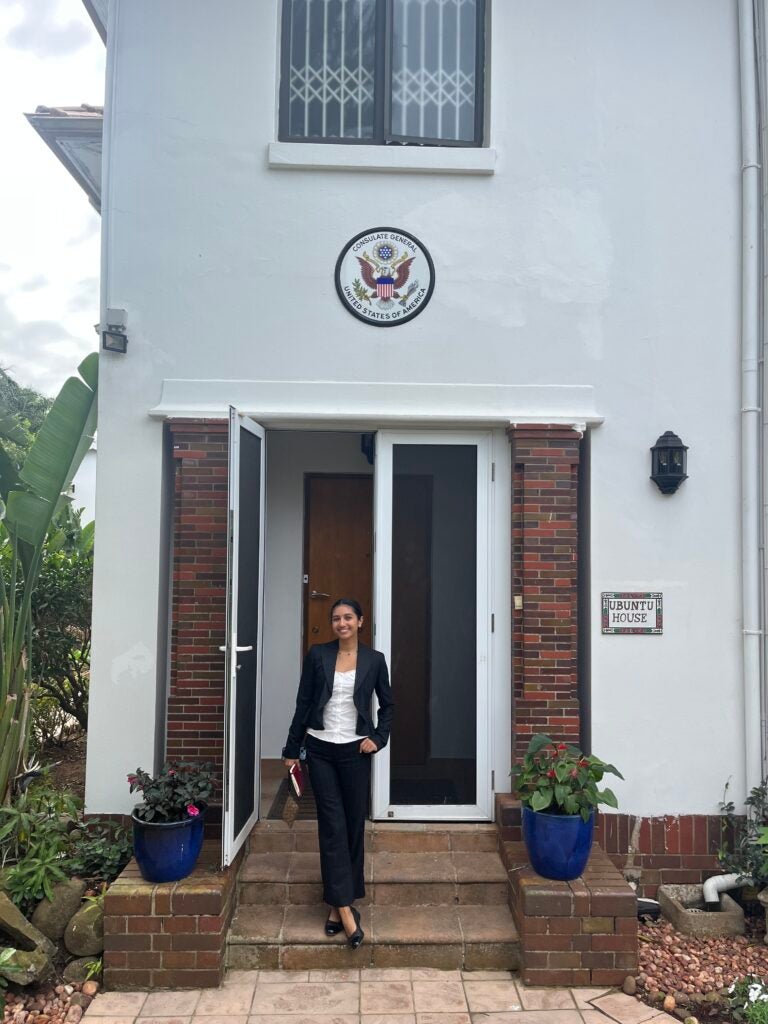 Girl stands in front of entryway of the US Consulate in Durban, a white building with bricks