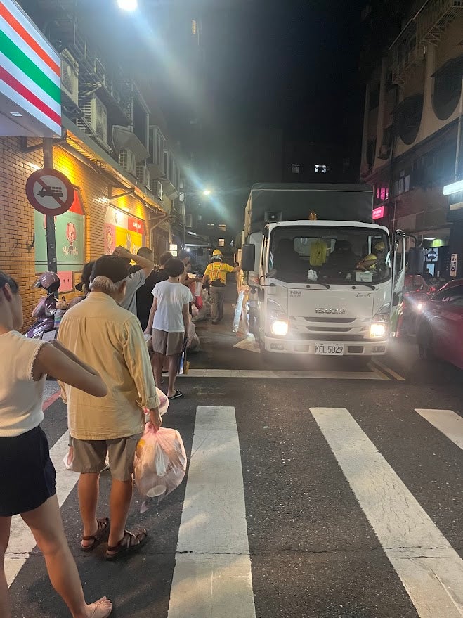 People lining up on the street waiting for a white truck to pick up their trash