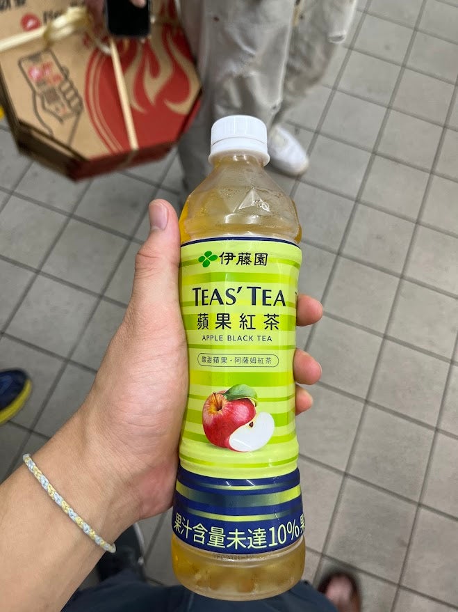 A hand holding a plastic tea bottle that reads "Teas' Tea" with an apple