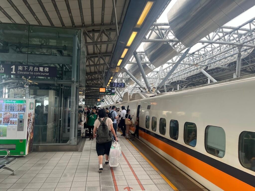 A white, black, and orange train with people waiting to enter