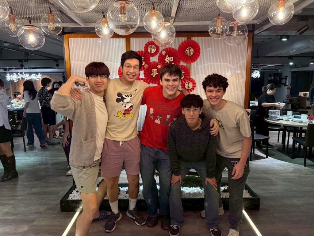 5 boys posing for a photo in front of a white divider with red decorations