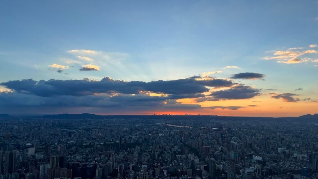 A tall perspective overlooking a cityscape, the clouds, and a sunset