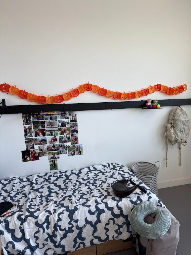 A twin-size bed with a photo collage on the wall and an orange wreath