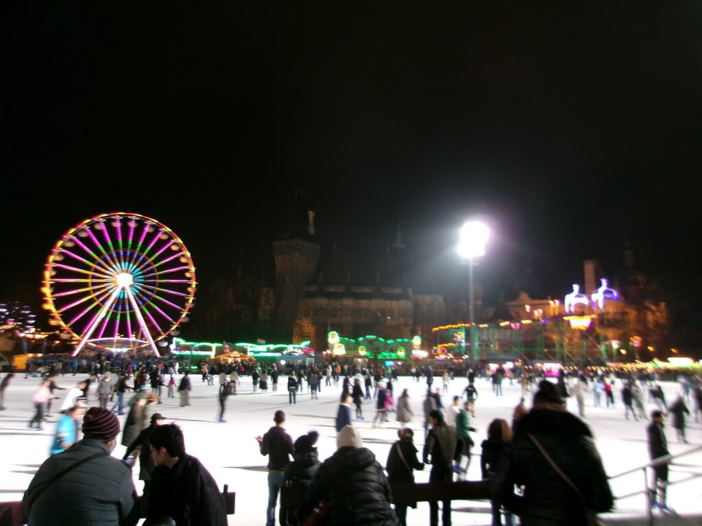 A busy, nighttime ice skating rank with neon lights from a ferris wheel and Christmas lights
