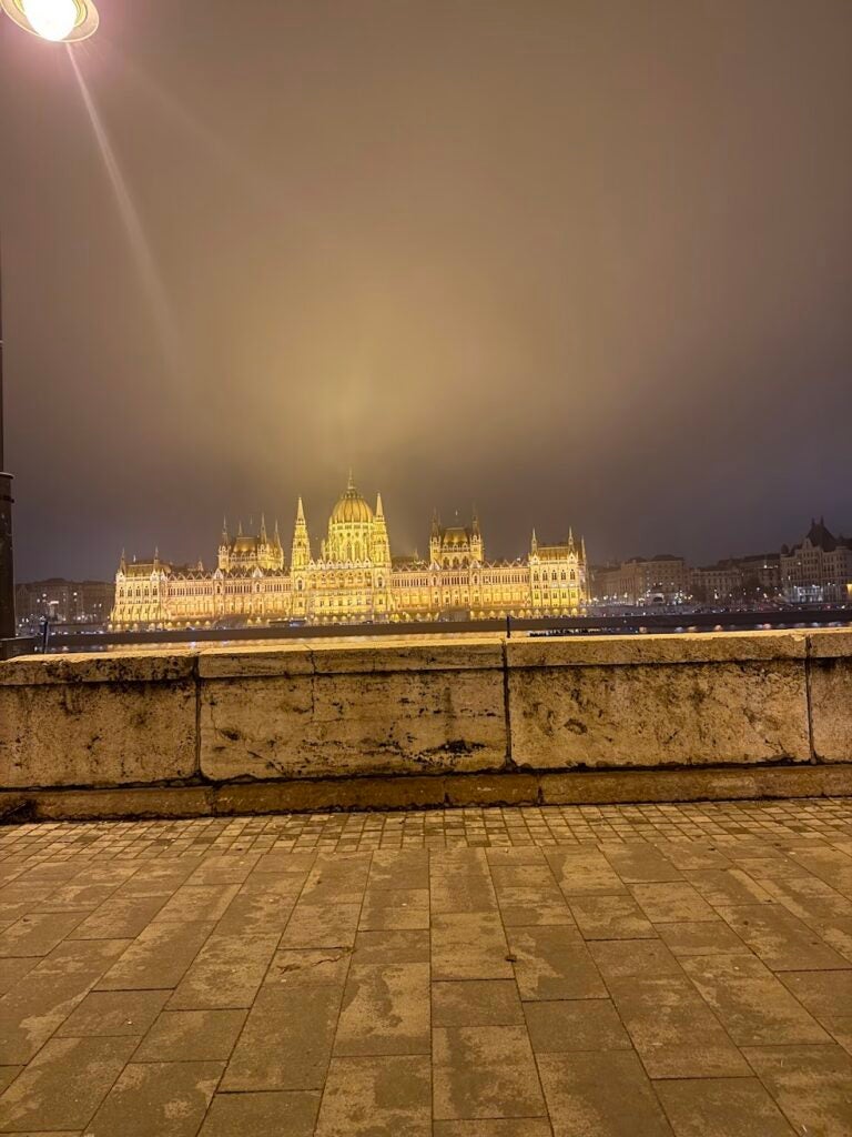 A night shot of the Hungarian Parliament building with lots of arches across a river